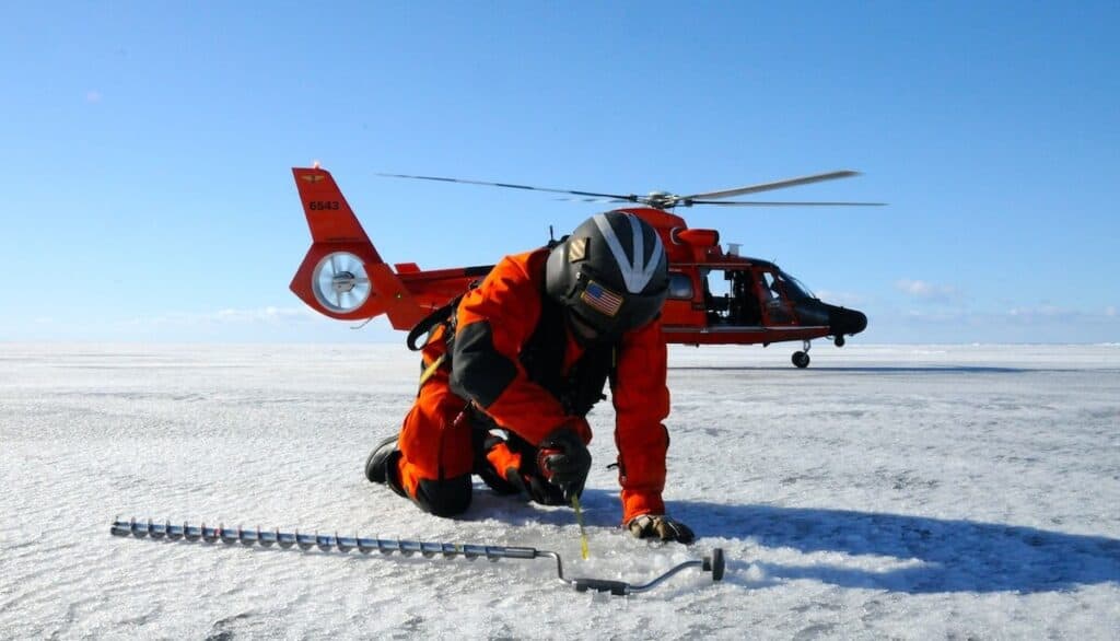 worker drilling for ice core samples on Lake Superior to study Lake Superior’s Weather with helicopter in the background